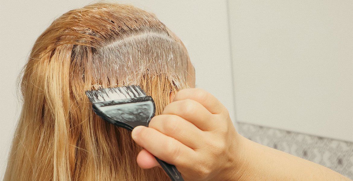 Mulher de cabelo claro pintando os fios com auxilio de um pincel